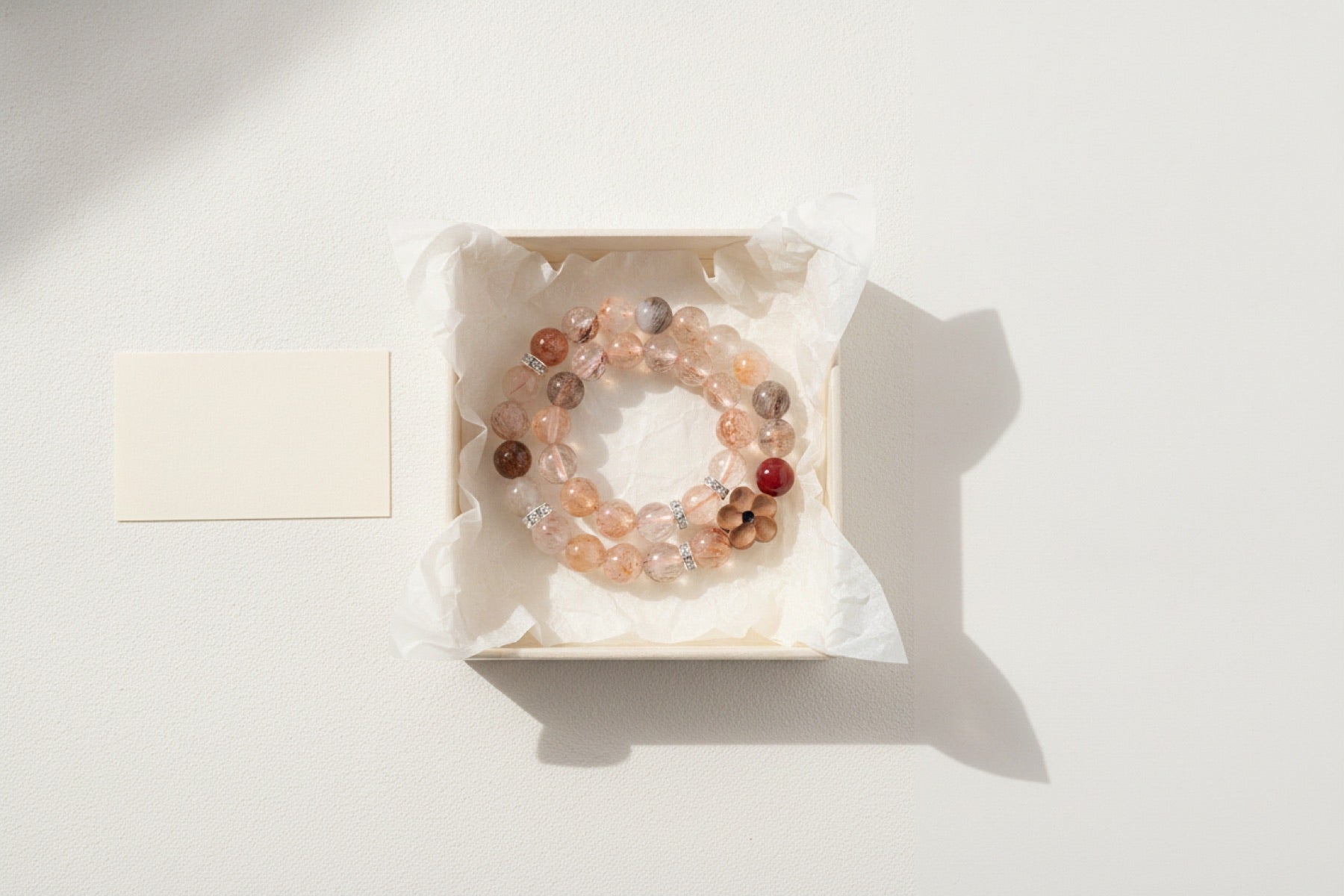 A crystal bracelet loosely coiled on acid-free tissue in a shallow specimen tray beside a blank ivory identification card