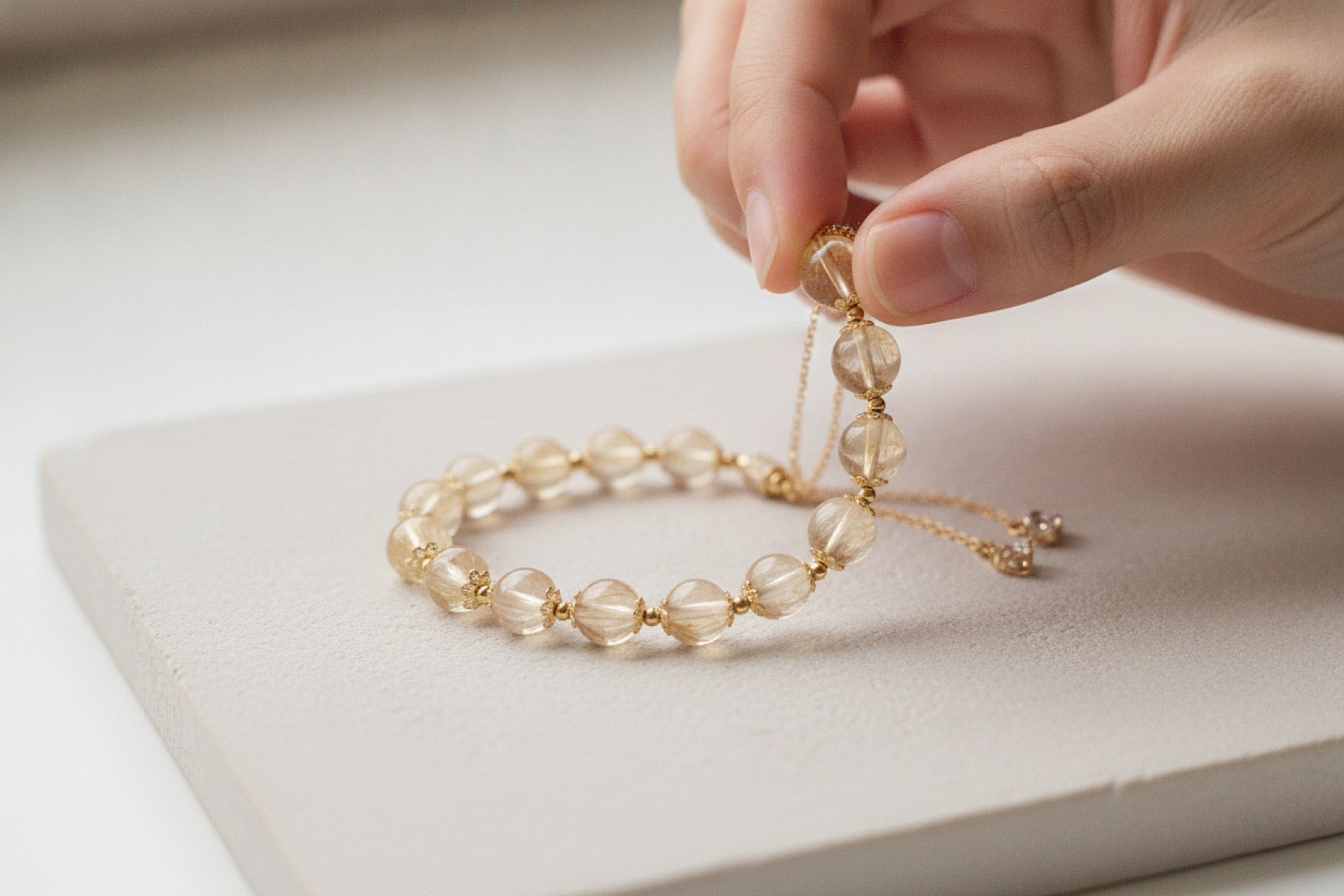Bare hands threading a round rutilated quartz bead onto a cord
